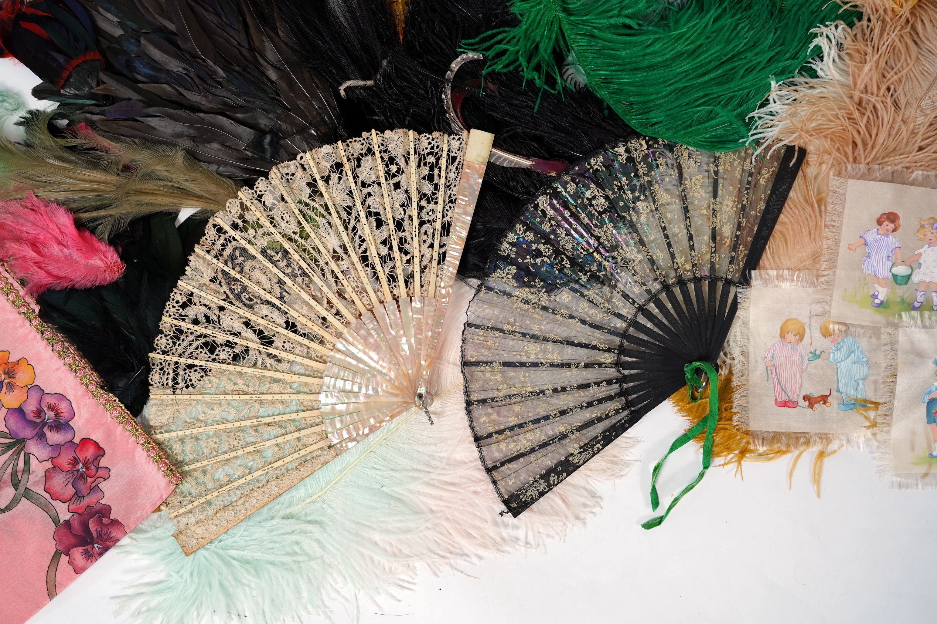 A collection of Edwardian exotic feather hat ornaments, with a collection of coloured ostrich feathers, two similar feather fans, a lace and another fan and silk hand painted mats